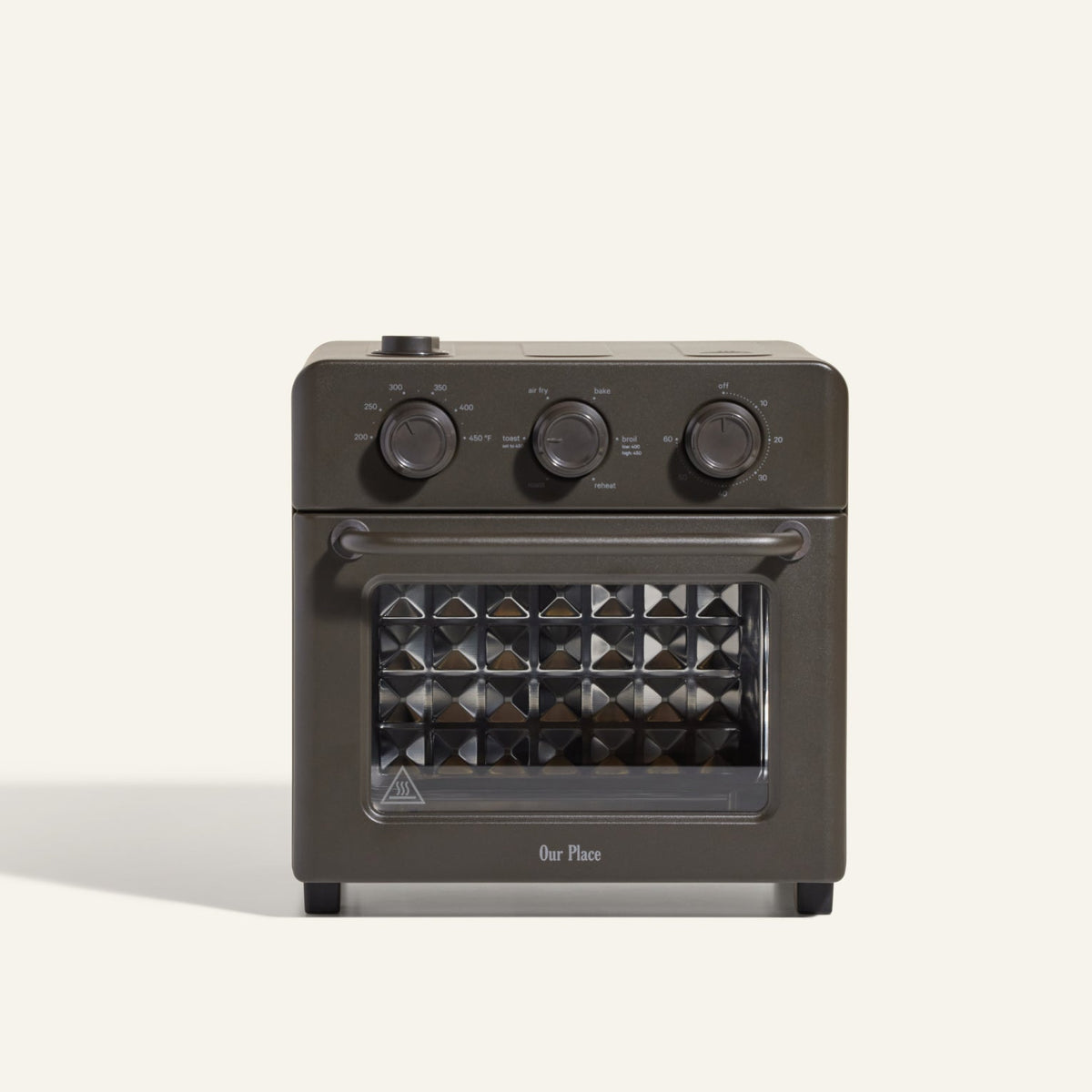 The AU - Wonder Oven is a dark gray countertop toaster oven with three top control dials and a front glass door featuring a diamond-patterned interior. "Our Place" appears at the bottom of the door. Doubles as an air fryer for extra versatility.